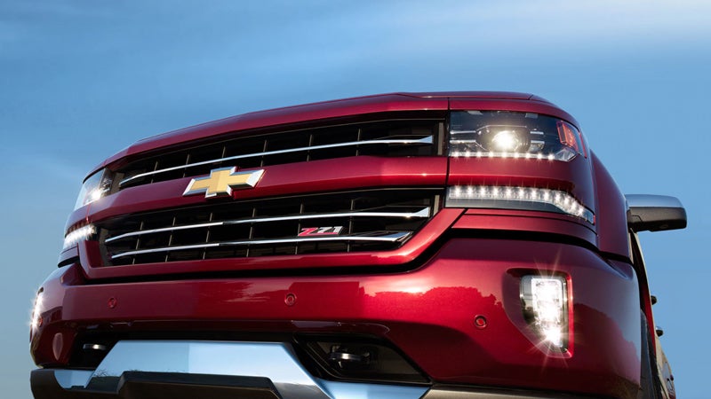 Close-up of the front grille of a red Chevrolet Silverado Z71 truck with LED headlights and fog lights shining.