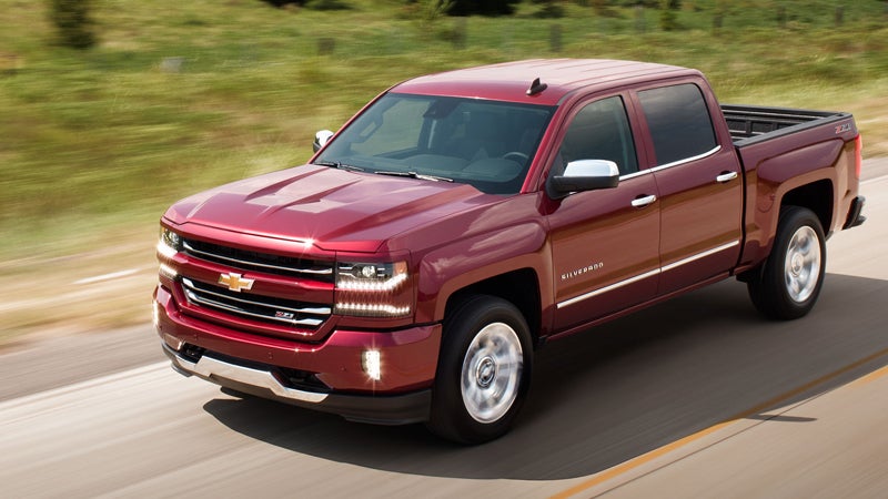 Side view of a red Chevrolet Silverado pickup truck driving on the highway.