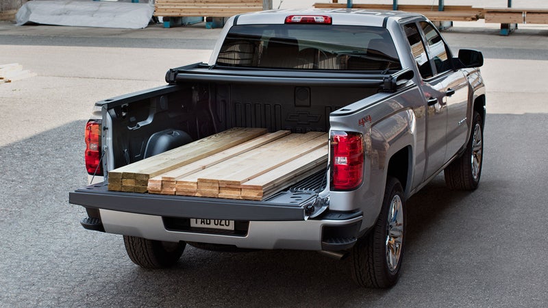 Rear view of a Chevrolet Silverado pickup truck with an open bed carrying wooden planks, parked in an industrial setting.