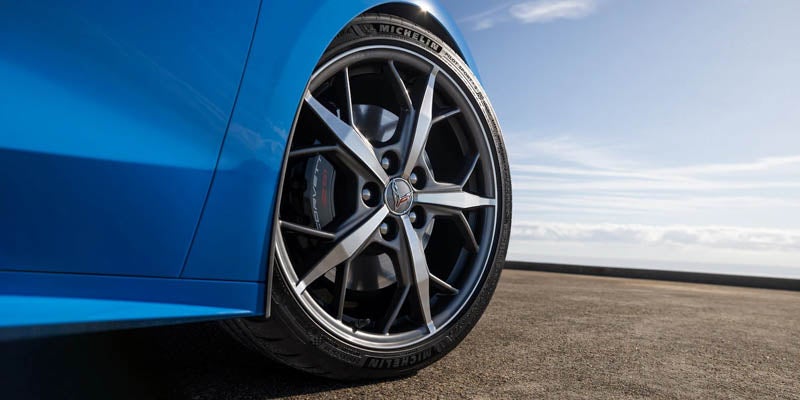Close-up of a Corvette wheel on a blue car with a coastal background.