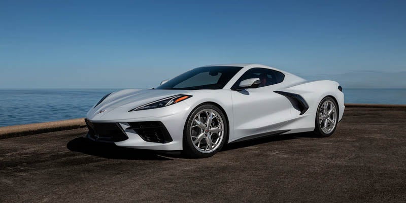 White Chevrolet Corvette parked near the ocean under a clear sky.