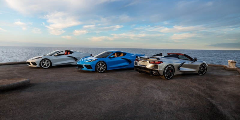 Three Chevrolet Corvette sports cars parked near the ocean at sunset.
